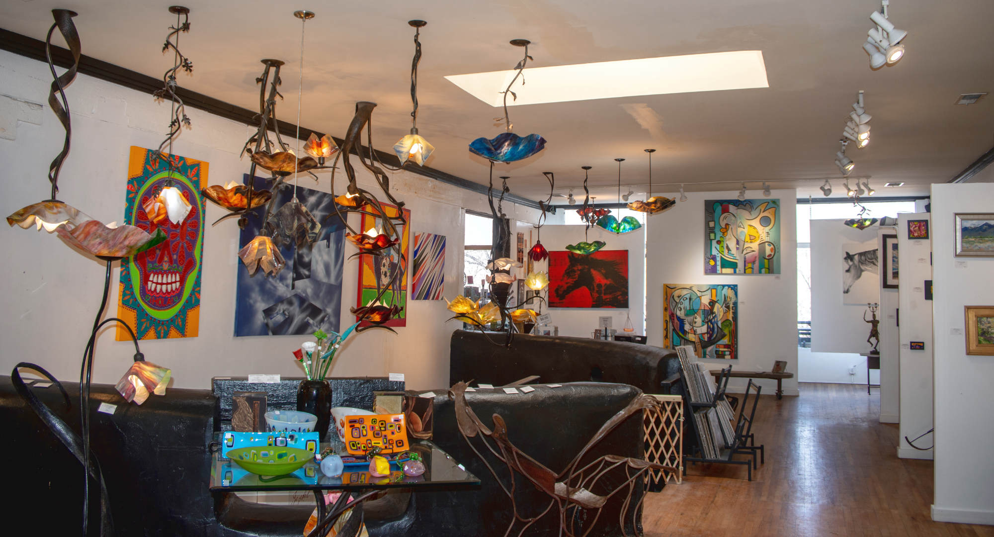 view of Jezebel Gallery, a art gallery in Madrid, New Mexico. image shows large slumped glass chandeliers and paintings on the walls